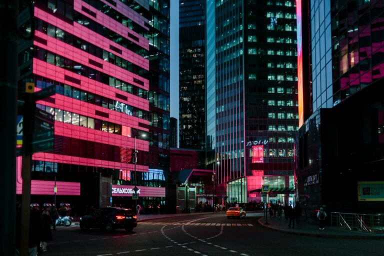 Vibrant city street at night with pink lights.