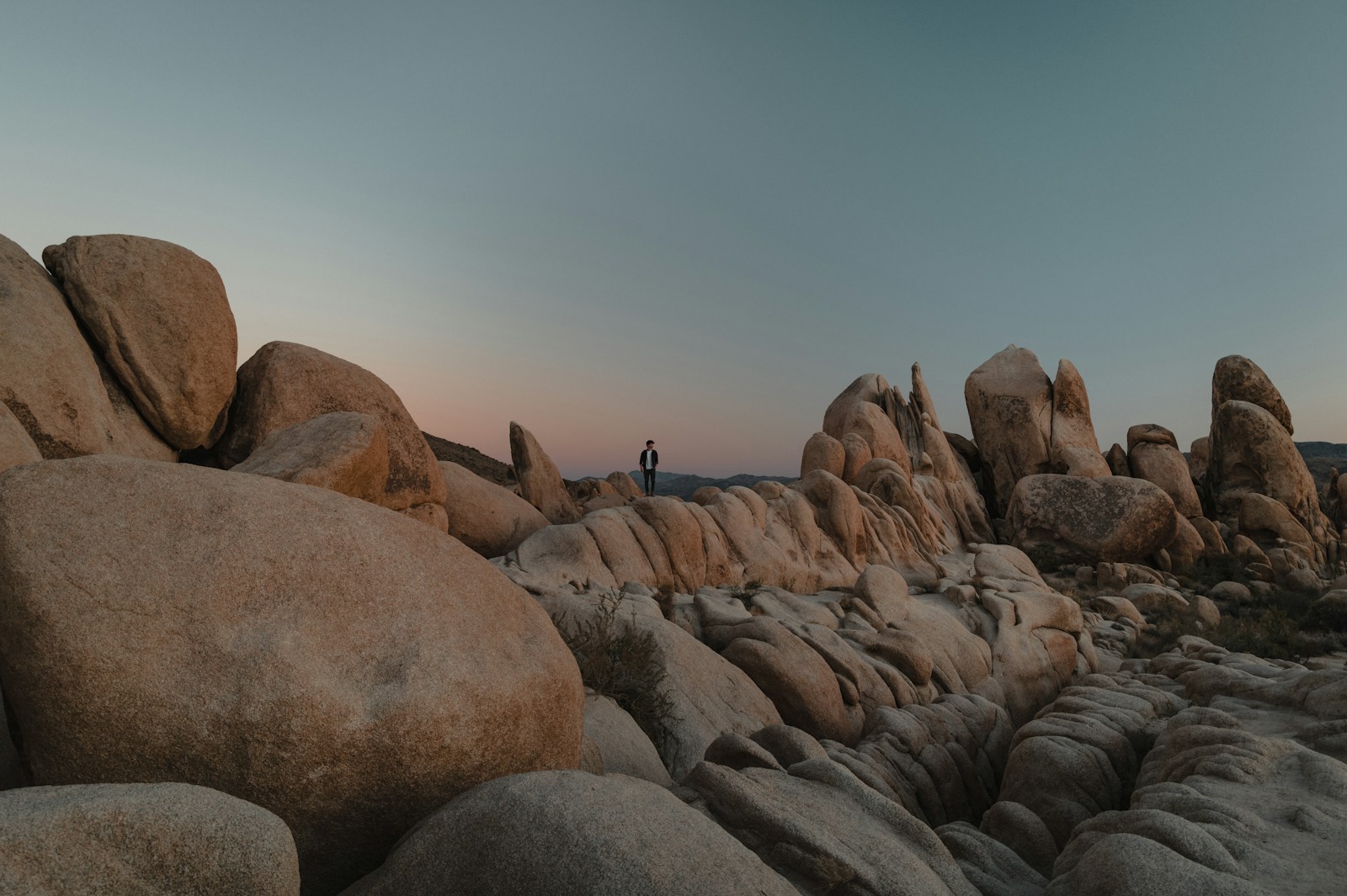 Person stands atop rocky landscape at dusk.